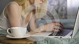 Young woman lying on bed using notebook computer and typing.