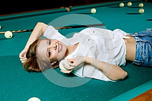 Young woman lying on the billiard table and looking at camera.