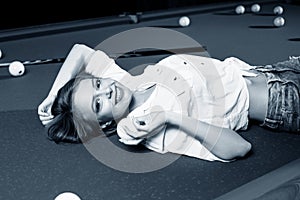 Young woman lying on the billiard table and looking at camera.