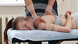 Young woman lying on a couch in the clinic and the massagist massaging her shoulder