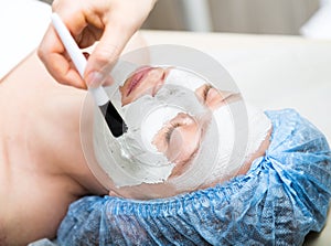 Young woman lying down in a spa salon and having a facial beauty treatment. The cosmetic procedures for the face. Beauty