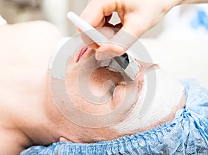 Young woman lying down in a spa salon and having a facial beauty treatment. The cosmetic procedures for the face. Beauty