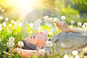 Young woman lying on the field in green grass and blowing dandelion