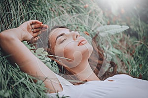 Young woman lying on the grass. Beauty woman lying on the field and looking on camera. Beautiful brunette Girl lying on the meadow