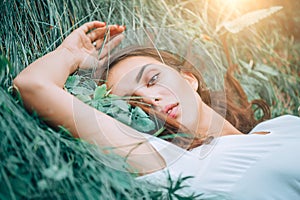 Young woman lying on the grass. Beauty woman lying on the field and looking on camera. Beautiful brunette Girl lying on the meadow