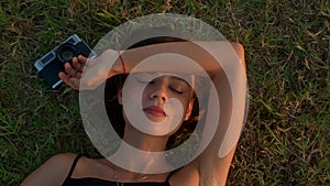 Young woman lying on the grass with retro camera