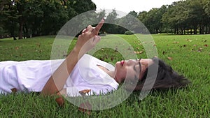 Young woman lying on the grass and sending sms, texting in the park.
