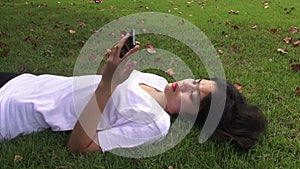 Young woman lying on the grass and sending sms, texting in the park.