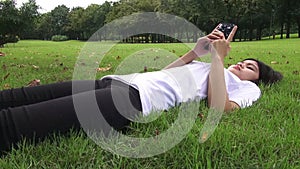 Young woman lying on the grass and sending sms, texting in the park.