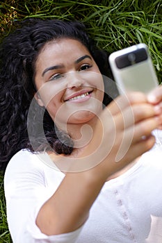 Young Woman Lying On Grass Sending Text Message