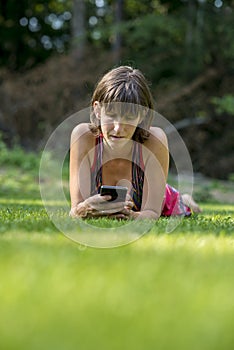 Young woman lying in green grass using her smart phone