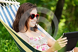 Young woman lying in a hammock in garden with E-Book.