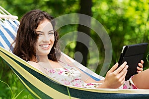 Young woman lying in a hammock in garden with E-Book.