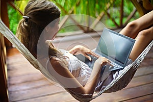 Young woman lying in a hammock with laptop in a tropical resort.