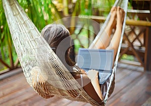 Young woman lying in a hammock with laptop in a tropical resort.