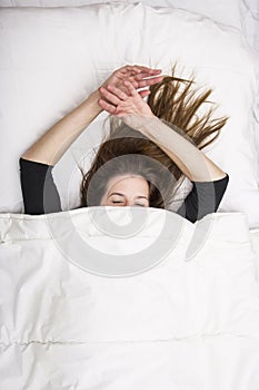 Young woman is lying in her bed with closed eyes, smiling under her blanket after a restful sleep. photo