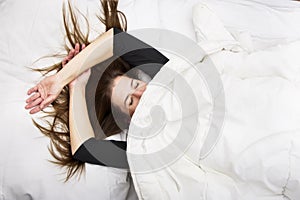 Young woman is lying in her bed with closed eyes, smiling under her blanket after a restful sleep.