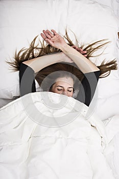 Young woman is lying in her bed with closed eyes, smiling under her blanket after a restful sleep. photo