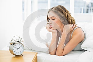 Young woman lying in her bed looking at the alarm clock