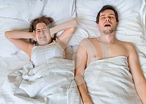 Young woman is lying with her husband in bed. Man is snoring too loud. Woman is covering her ears