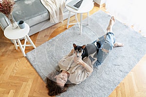 Young woman lying at home on living room carpet with her Basenji dog. Lifestyle and love for pets