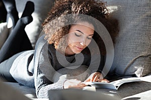 Young woman lying on lounge reading magazine