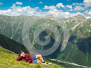 Young woman lying in a meadow with flowers in front of the North Caucasus mountain range