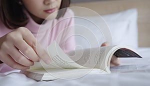 Young woman lying and reading book on bed