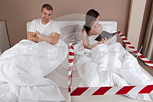 Young woman lying separately from husband on the bed and reading