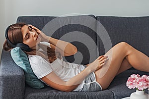 Young woman lying on the sofa in the headphones with her eyes closed relaxing, listening to calm music