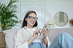 A young woman is lying on the sofa at home and smilingly using a mobile phone photo