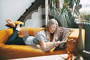 A young woman is lying on the sofa and reading a favorite book. The girl is resting, devotes her free time to reading