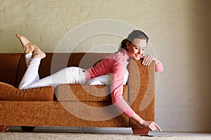 Young woman lying on sofa using digital tablet