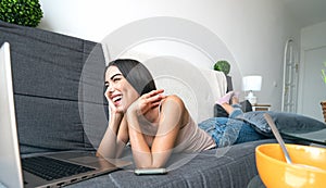 Young woman lying on sofa watching on computer - Happy girl having fun using laptop at home