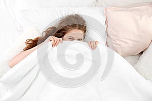 Young woman lying on soft pillows and hiding under blanket
