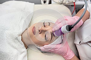 Young woman lying at spa salon and receive cleaning procedure on face with ultrasound hardware