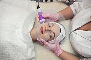 Young woman lying at spa salon and receive cleaning procedure on face with ultrasound hardware