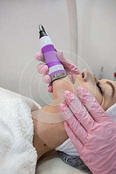 Young woman lying at spa salon and receive cleaning procedure on face with ultrasound hardware