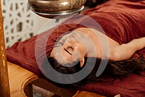 Young woman lying under shirodhara vessel during ayurvedic procedure