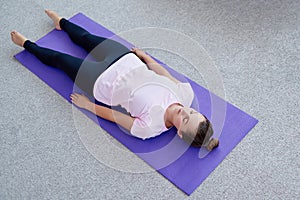 Young woman lying on yoga mat with eyes closed in savasana pose at home. Fitness, sport and healthy lifestyle concept. Corpse pose