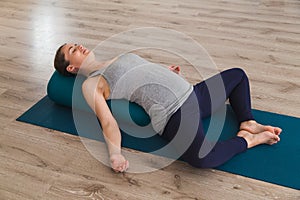 Young woman lying on yoga mat using bolster cushion