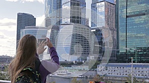 Young woman make a photo of high skyscraper using smartphone mobile cell phone camera.