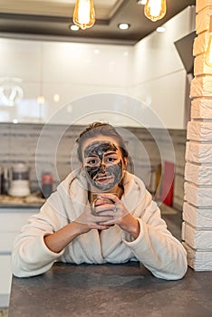 young woman makes herself a black clay regenerating mask that smoothes wrinkles.