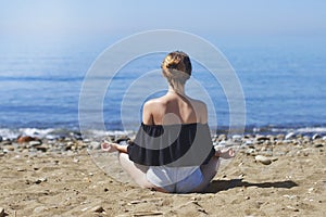 Young woman makes meditation in lotus pose on sea / ocean beach, harmony and contemplation. Beautiful girl practicing yoga at sea