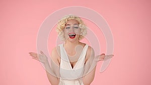 Young woman makes a victory gesture, celebrating her triumph. A woman in the look of Marilyn Monroe in the studio on a