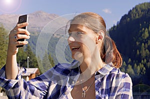 A young woman makes a video call with her cellphone and greets someone in the mountain