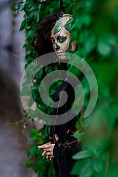 Young woman with Makeup of green skull for halloween surrounded by green leafs