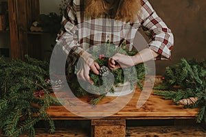 Young woman making Christmas floral arrangement. DIY Christmas table decoration.