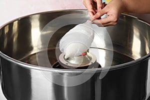 Young woman making cotton candy with modern machine on pink background