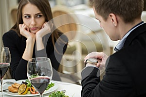 Young woman making an exasperated expression gesture on a bad date at the restaurant. Man looks at his watch.